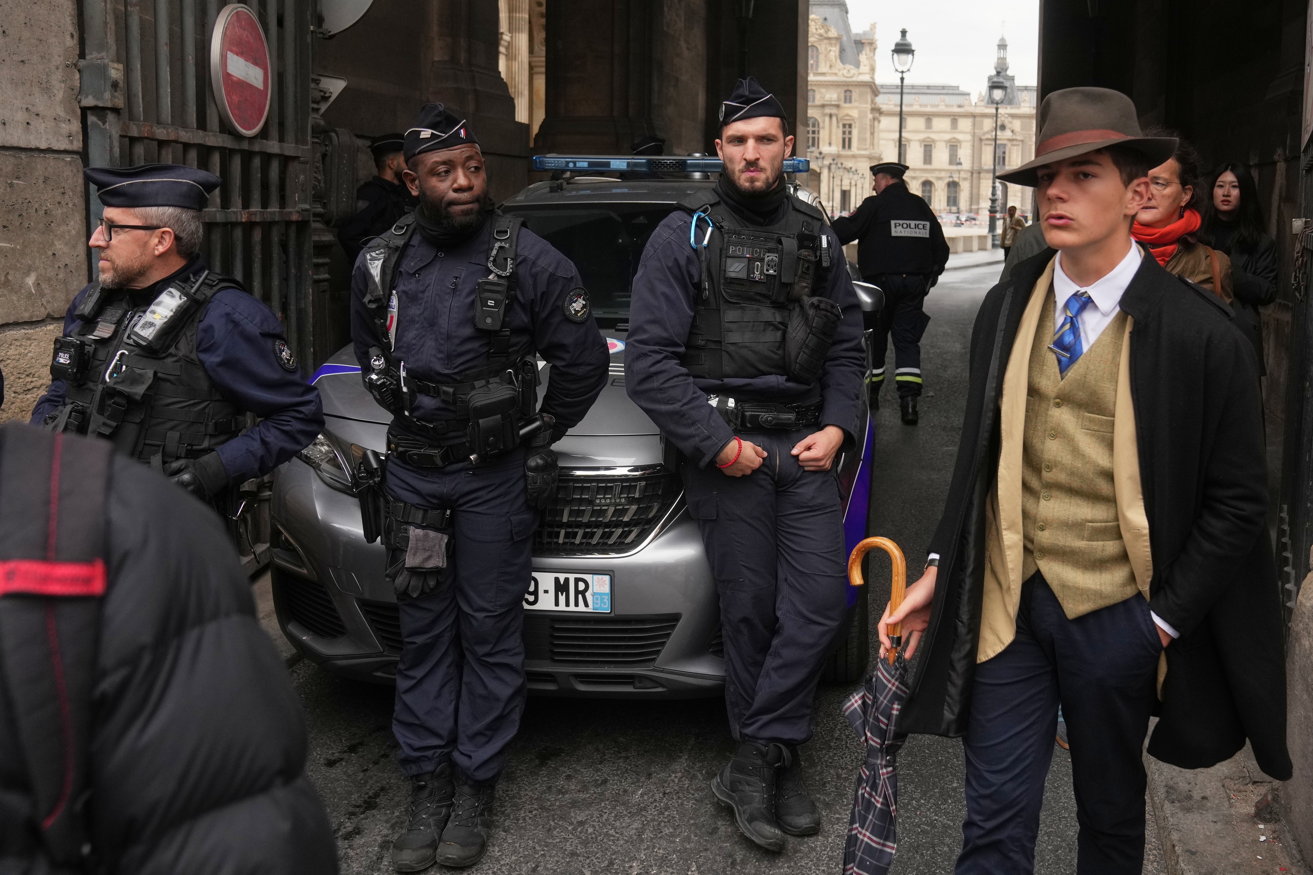 Pedro Elias Garzon Delvaux, right, walks past as police officers block an entrance to the Louvre after thieves carried out a daylight raid on French crown jewels, in Paris, Oct. 19, 2025.